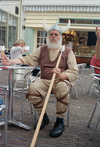 818910 Afbeelding van een uitrustende Viking, gespeeld door Frans van Rijnswou (ca. 1951-2009) op een terras met een ...